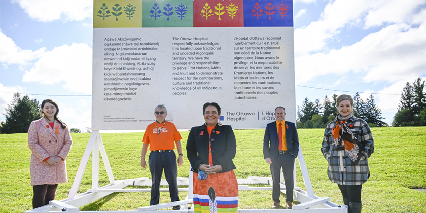 Members of The Ottawa Hospital staff and Indigenous partners stand in front of a land acknowledgement sign that features Indigenous artwork