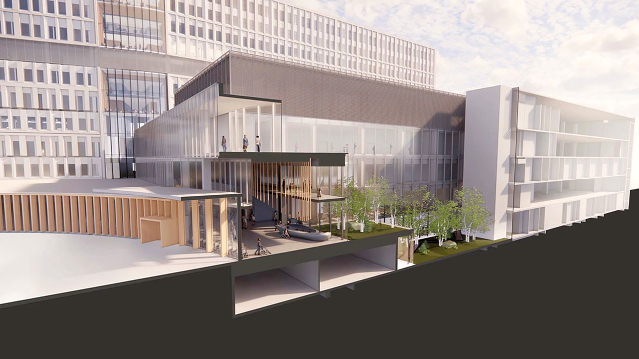 An artist rendering of a cross section perspective of the main concourse inside the new hospital. An information desk is positioned in front of large windows, showing a clear view to the outdoors. The main hospital building is in the background behind the concourse.