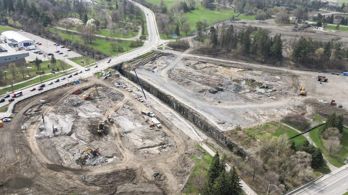 An aerial view in spring of the construction site where the parking garage for The Ottawa Hospital’s new campus will be built. Construction crews are excavating the ground with backhoes and other heavy equipment.