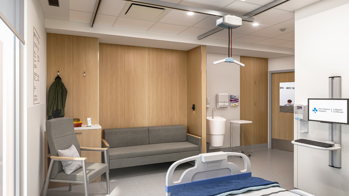 An artist rendering of the inside of a patient room at a new hospital, from the perspective of one corner of the room next to the patient bed. Moving left to right on the opposite wall of the room, there is a chair and sofa, a sink, a door with a window showing a member of hospital staff in the hallway outside, and a computer monitor and keyboard next to a hand sanitizer dispenser.